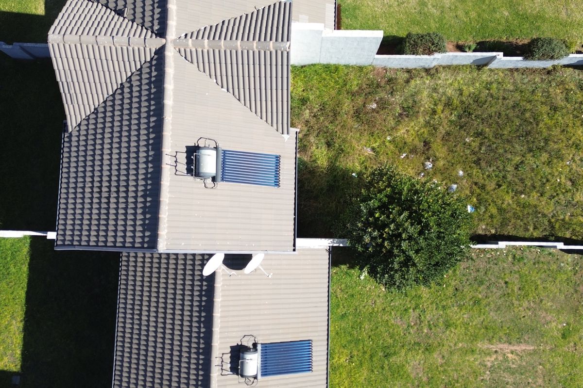 Aerial view of the townhouse roof featuring installed solar water heating systems, satellite dishes, and surrounding garden space with boundary walls.