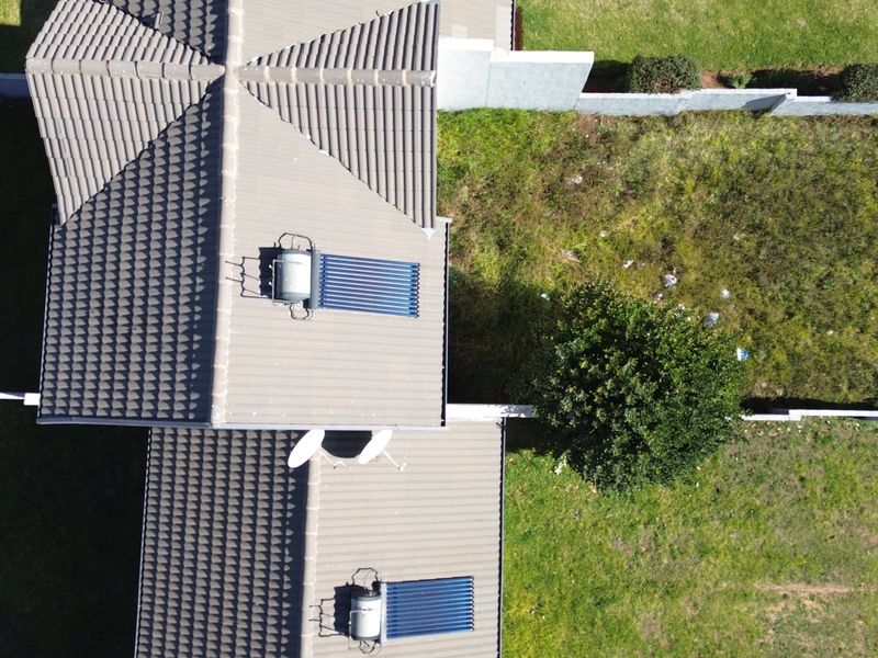 Aerial view of the townhouse roof featuring installed solar water heating systems, satellite dishes, and surrounding garden space with boundary walls.