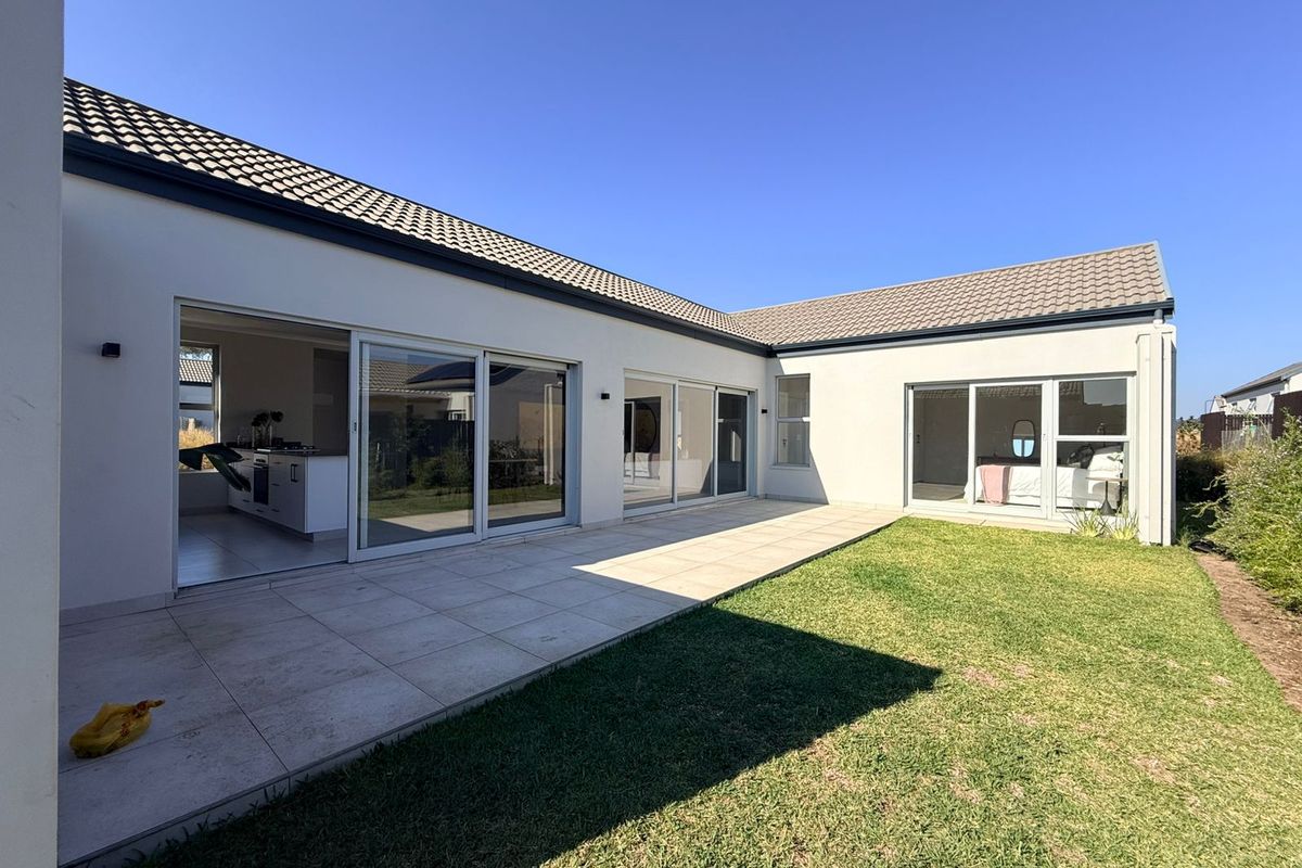 Rear view of the property featuring a paved patio area, well-maintained lawn, and large sliding glass doors providing seamless indoor-outdoor flow.