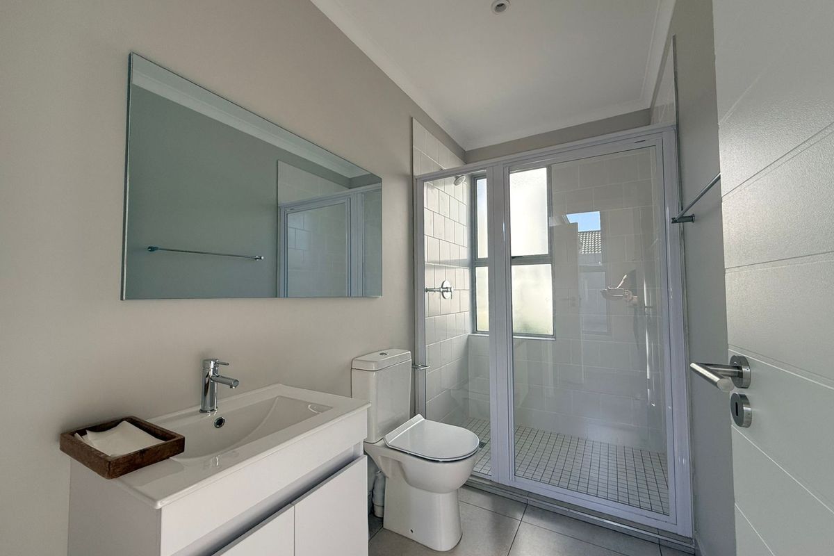 A clean, modern bathroom featuring a vanity cabinet with basin, a toilet, and a glass-enclosed shower with tiled finishes.