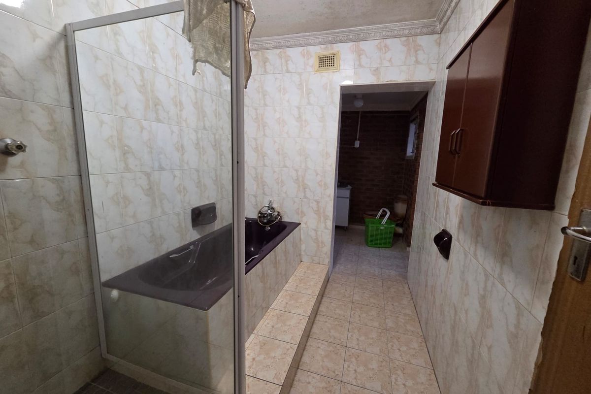 A dated bathroom featuring a built-in bathtub with a glass screen, tiled walls and floors, and wall-mounted storage cabinetry.