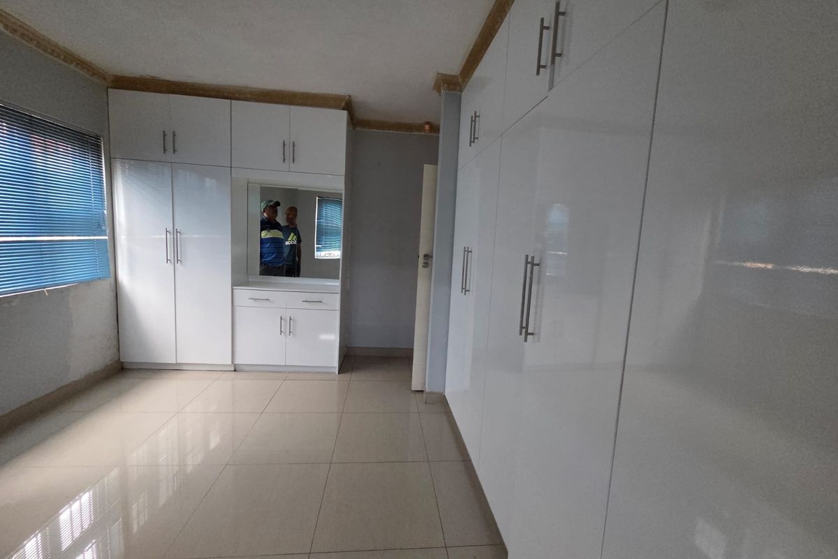A spacious bedroom featuring extensive white built-in cupboards, tiled flooring, and venetian blinds, offering ample storage and a clean, neutral aesthetic.