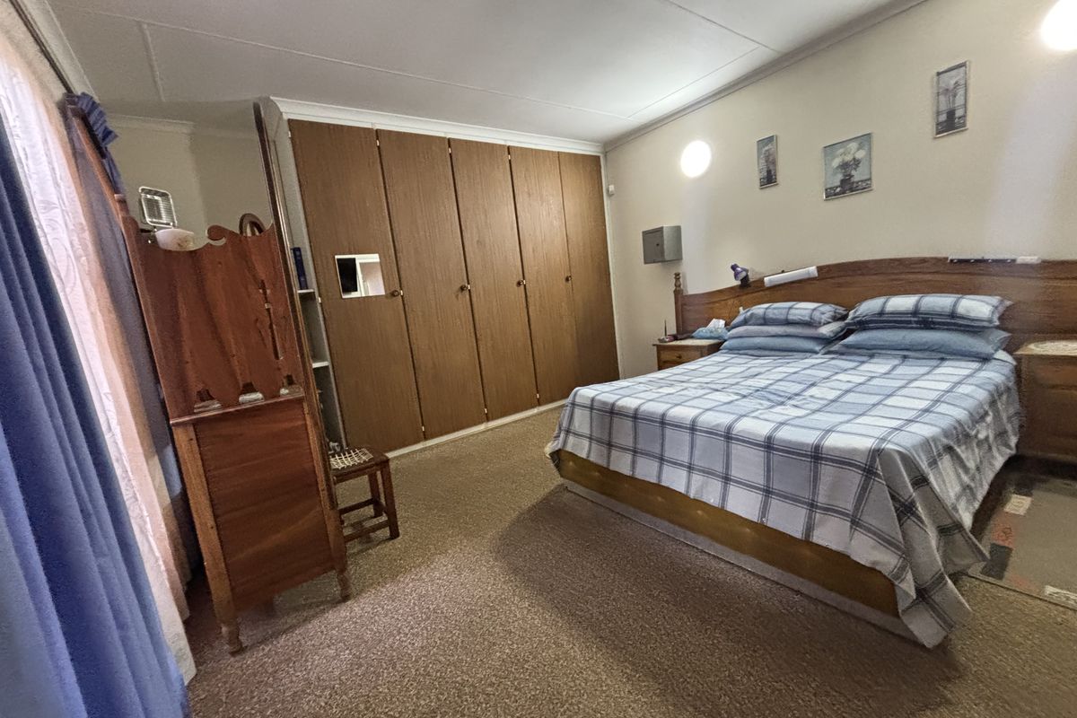 A spacious bedroom featuring wall-to-wall built-in wooden cupboards and carpeted flooring, offering a functional and traditional layout.