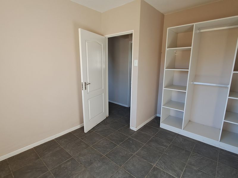 A clean, empty bedroom featuring tiled flooring and built-in wardrobe storage with open shelving.