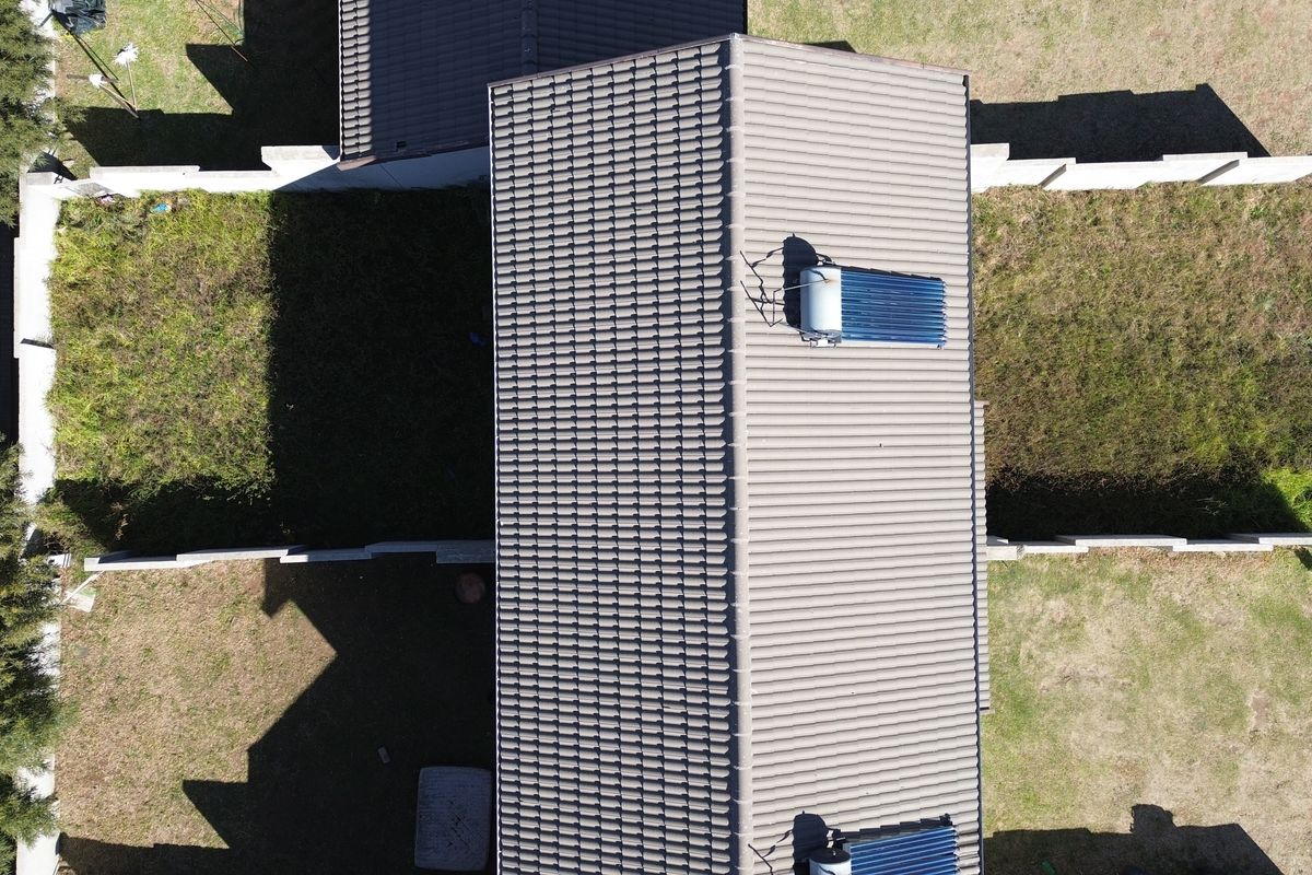 Aerial view of the townhouse property featuring a tiled roof with solar water heating panels and surrounding garden space with boundary walls.