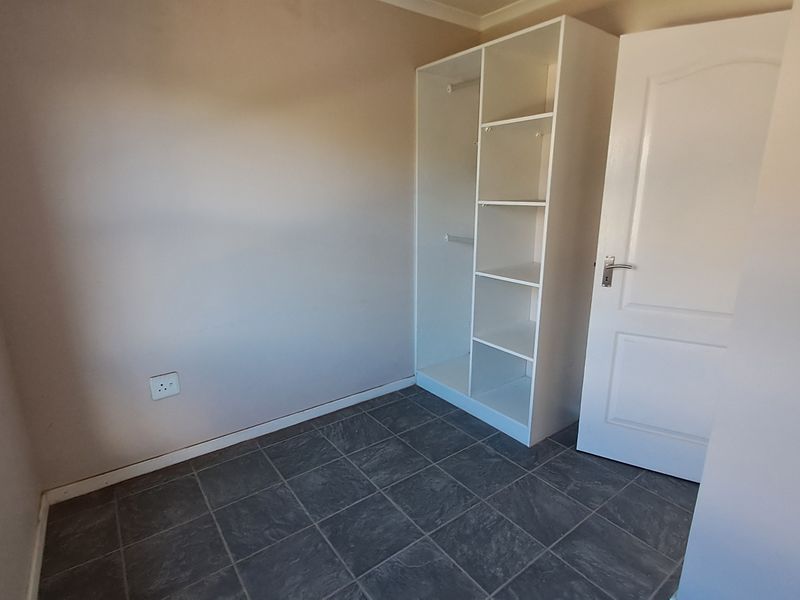 A simple, empty bedroom featuring tiled flooring and built-in shelving units, providing a clean and functional space ready for personalization.