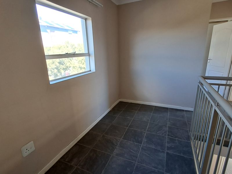 An empty upper-level landing area featuring dark tiled flooring, a metal balustrade, and a window providing natural light.