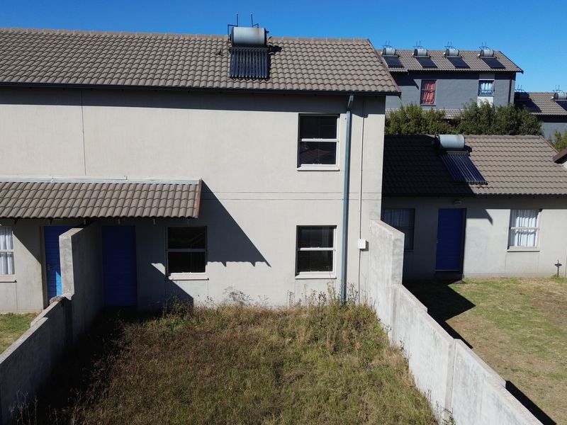 Aerial view of the rear exterior of a townhouse featuring a tiled roof, solar water heating system, and a private garden area with boundary walls.