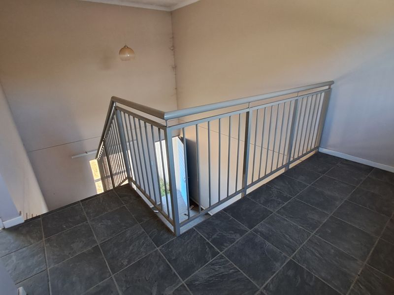 An empty upper-level landing area featuring dark tiled flooring and a metal balustrade overlooking the staircase.