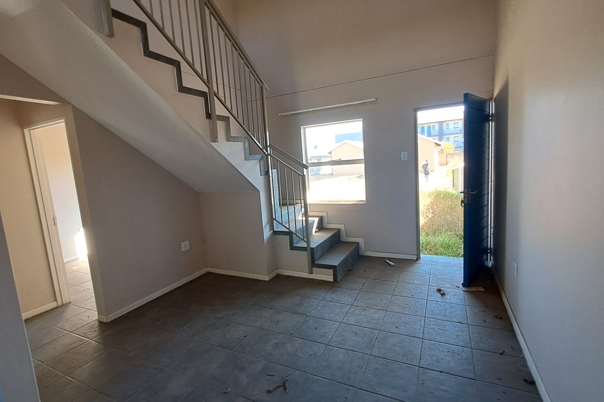 An open-plan living area featuring tiled flooring and a staircase with a metal balustrade, providing direct access to the exterior.