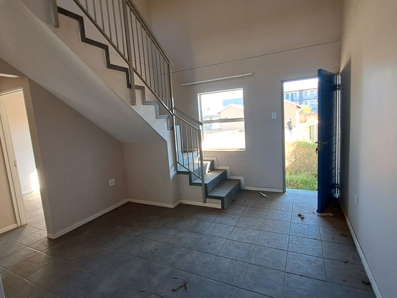 An open-plan living area featuring tiled flooring and a staircase with a metal balustrade, providing direct access to the exterior.