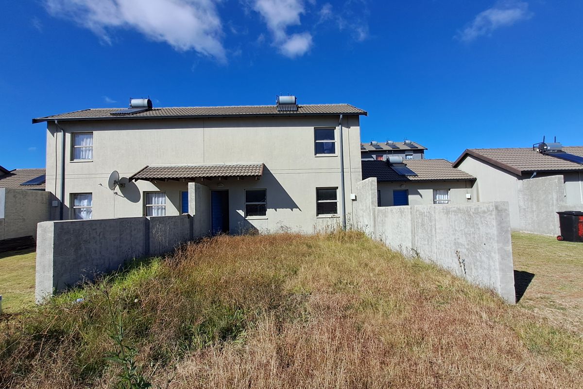Rear view of a two-story townhouse featuring a private yard with concrete boundary walls and solar water heating infrastructure on the roof.