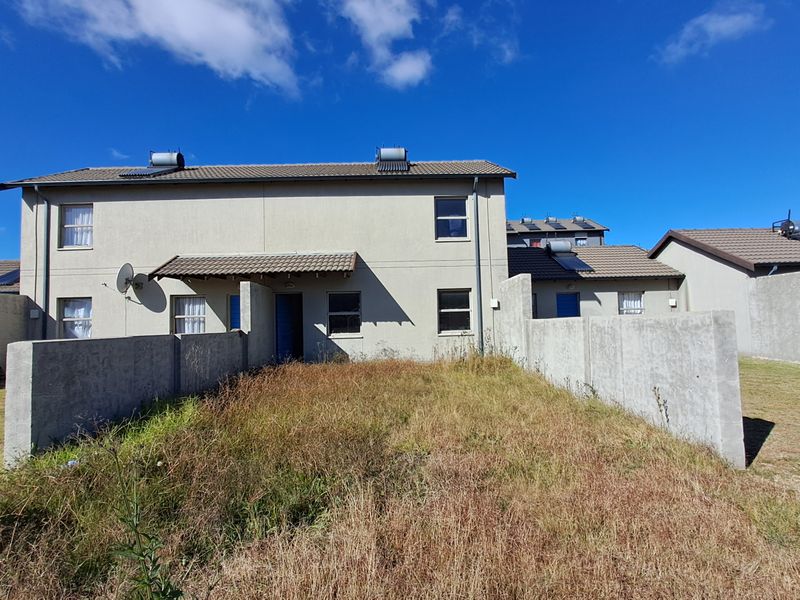 Rear view of a two-story townhouse featuring a private yard with concrete boundary walls and solar water heating infrastructure on the roof.