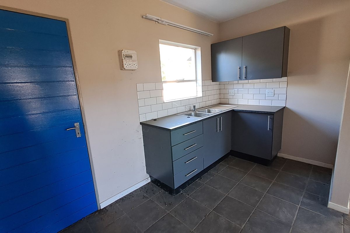 A compact kitchen area featuring grey built-in cabinetry, subway tile backsplash, and tiled flooring, currently vacant and ready for updates.