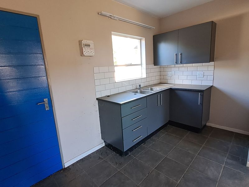 A compact kitchen area featuring grey built-in cabinetry, subway tile backsplash, and tiled flooring, currently vacant and ready for updates.