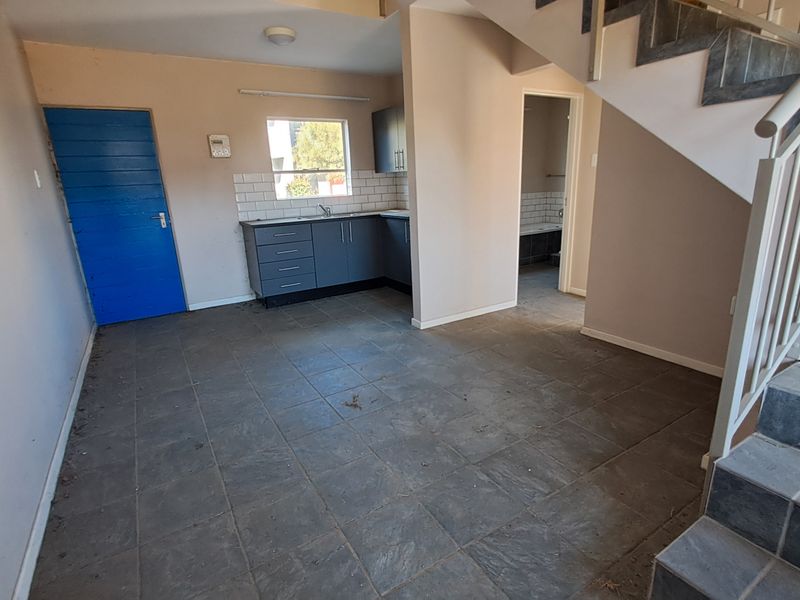 Open-plan living area featuring tiled flooring, a compact kitchen with built-in cabinetry, and a staircase leading to the upper level.