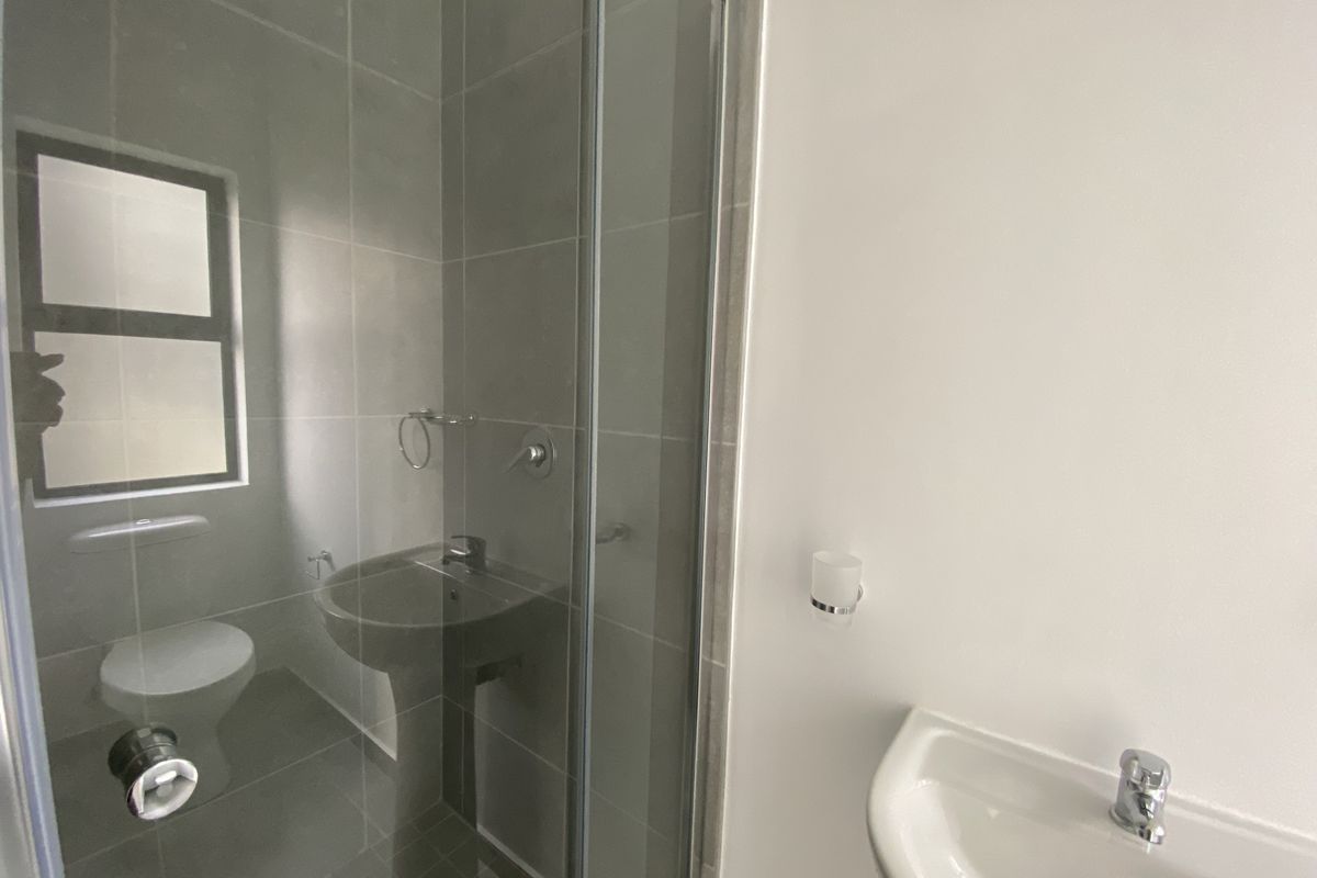 A clean, modern bathroom featuring a glass-enclosed shower, pedestal basin, and tiled finishes, presenting a well-maintained and functional space.