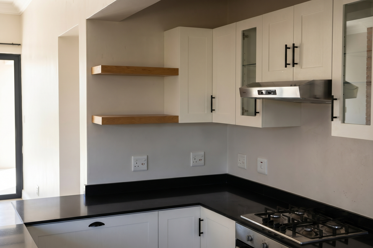 Modern kitchen featuring white cabinetry, black granite countertops, a gas hob with extractor fan, and floating wooden shelves, with direct access to the patio.