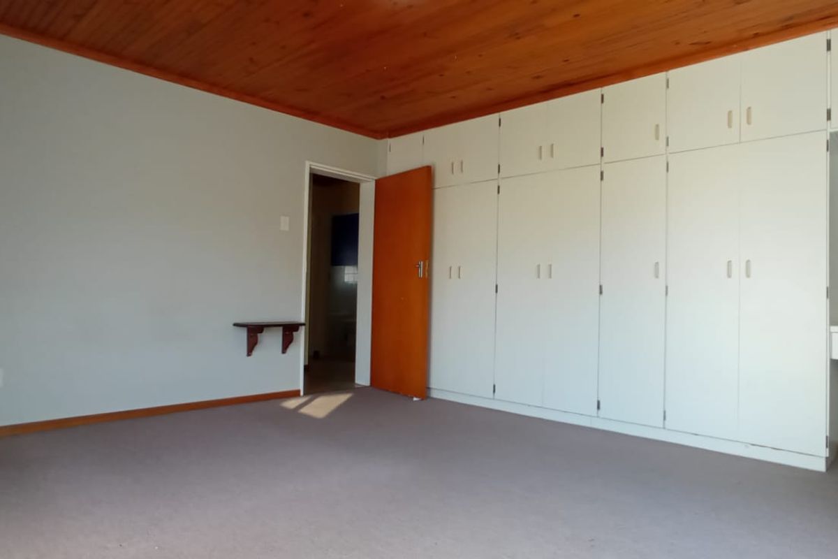 Spacious bedroom featuring extensive built-in cupboards, a vanity area, and a warm timber ceiling, offering a clean and functional living space.