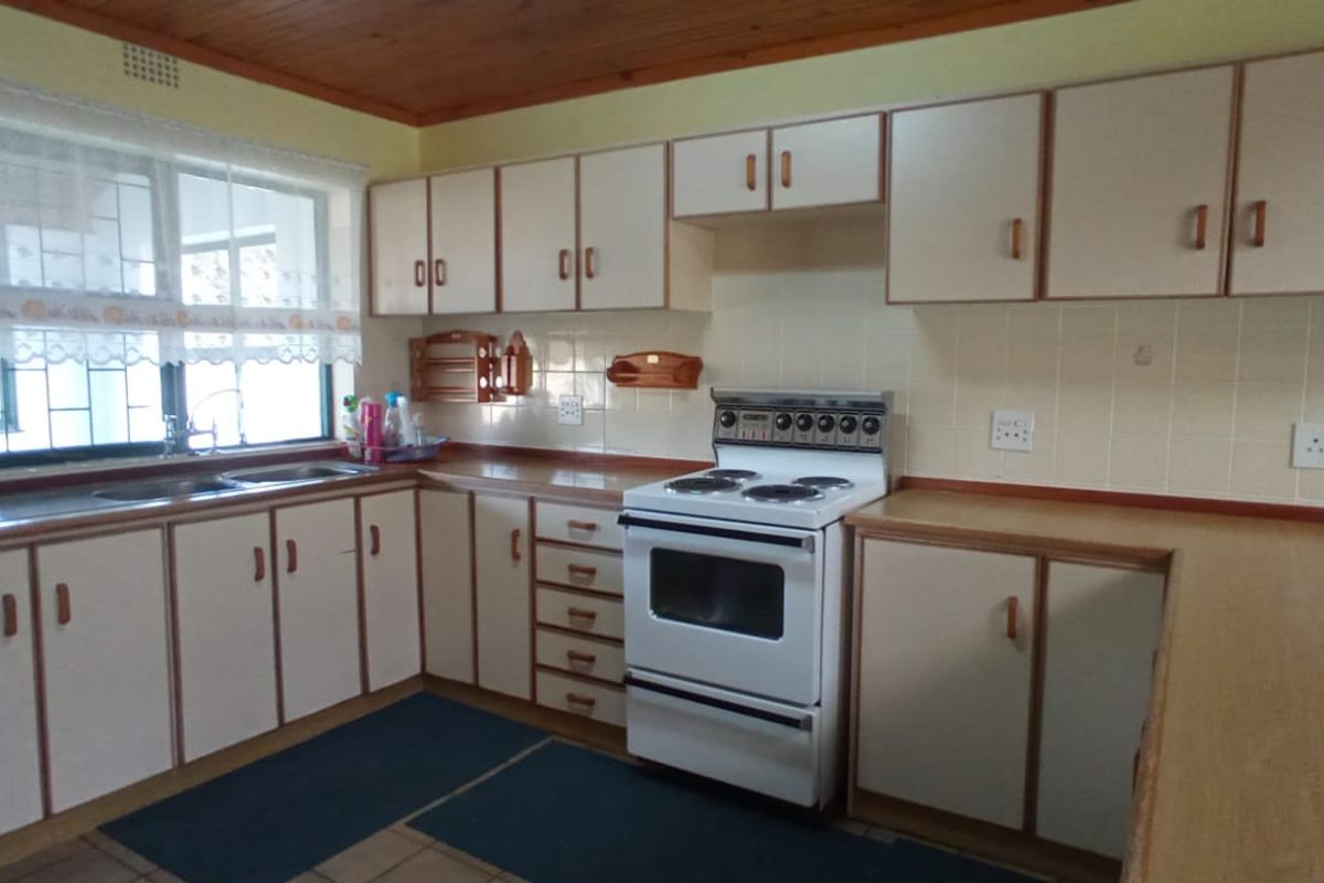A functional kitchen featuring timber ceiling, laminate countertops, tiled backsplash, and ample built-in cabinetry with a freestanding stove.