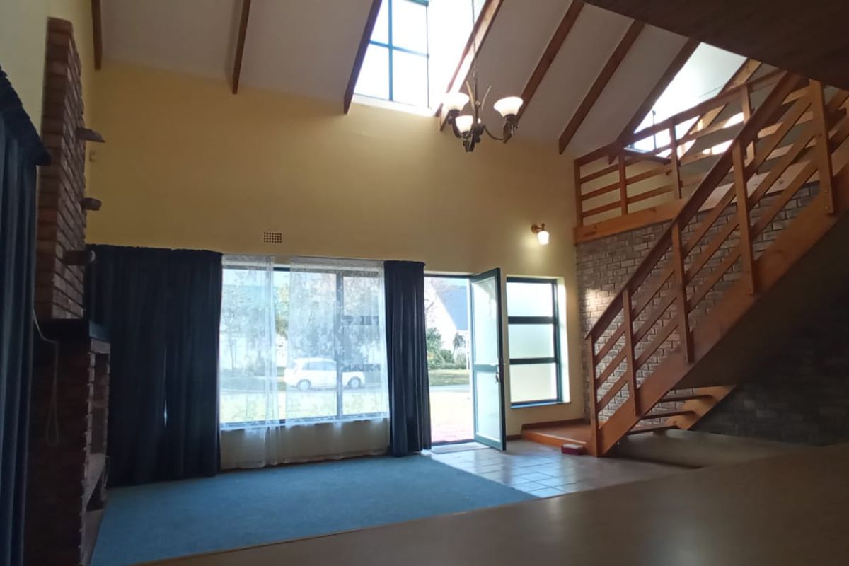 Spacious living area featuring a vaulted ceiling with exposed timber beams, a brick fireplace, and a timber staircase leading to an upper level.
