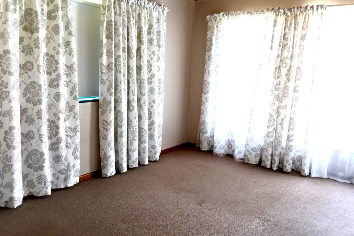 An empty bedroom featuring carpeted flooring, timber ceiling accents, and large windows with curtains.