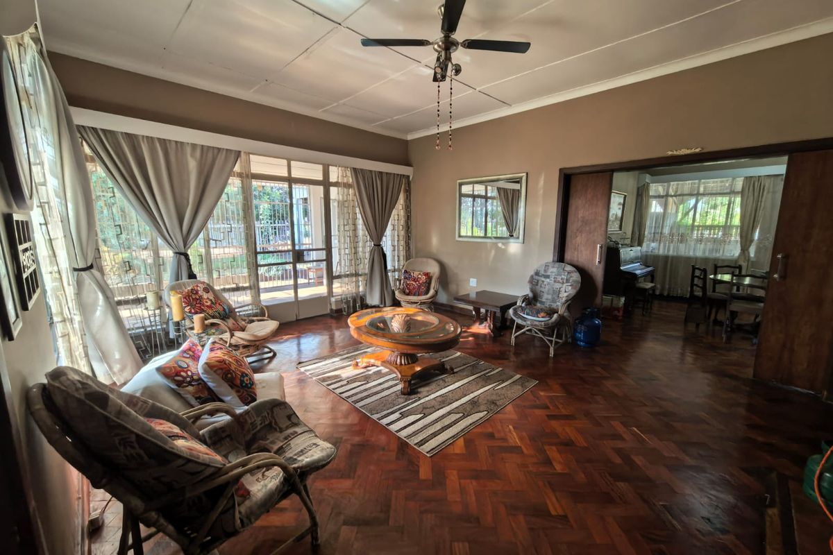 Spacious living room featuring classic parquet flooring, a ceiling fan, and large windows providing natural light with access to an adjoining dining area.