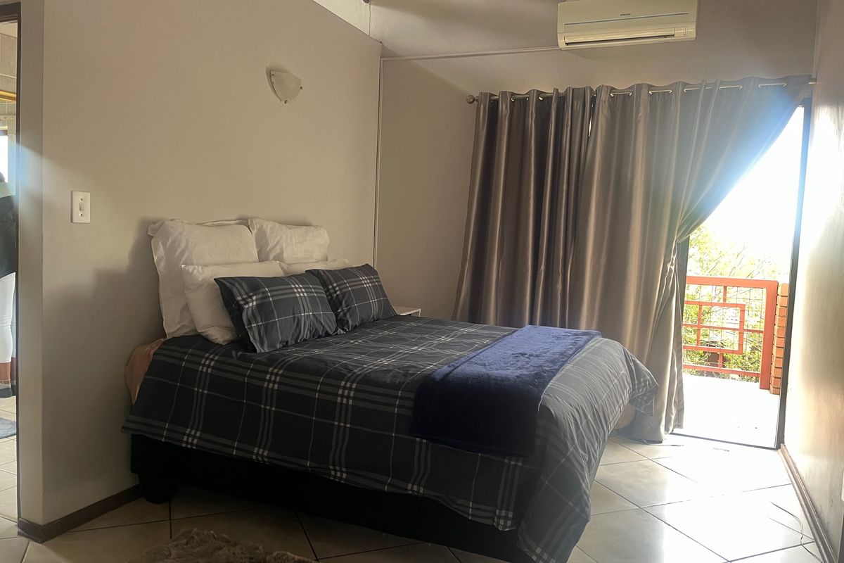 A bedroom featuring tiled flooring, vaulted ceilings, and a wall-mounted air conditioning unit, with direct access to an outdoor balcony area.