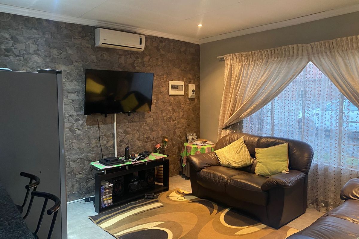 A living room featuring a textured stone-cladding feature wall, split-system air conditioning unit, and recessed downlighting.