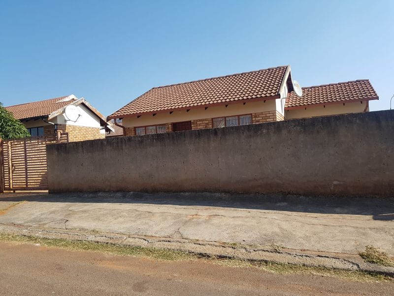 Front view of a residential property featuring a brick boundary wall, tiled roof, and concrete driveway access.