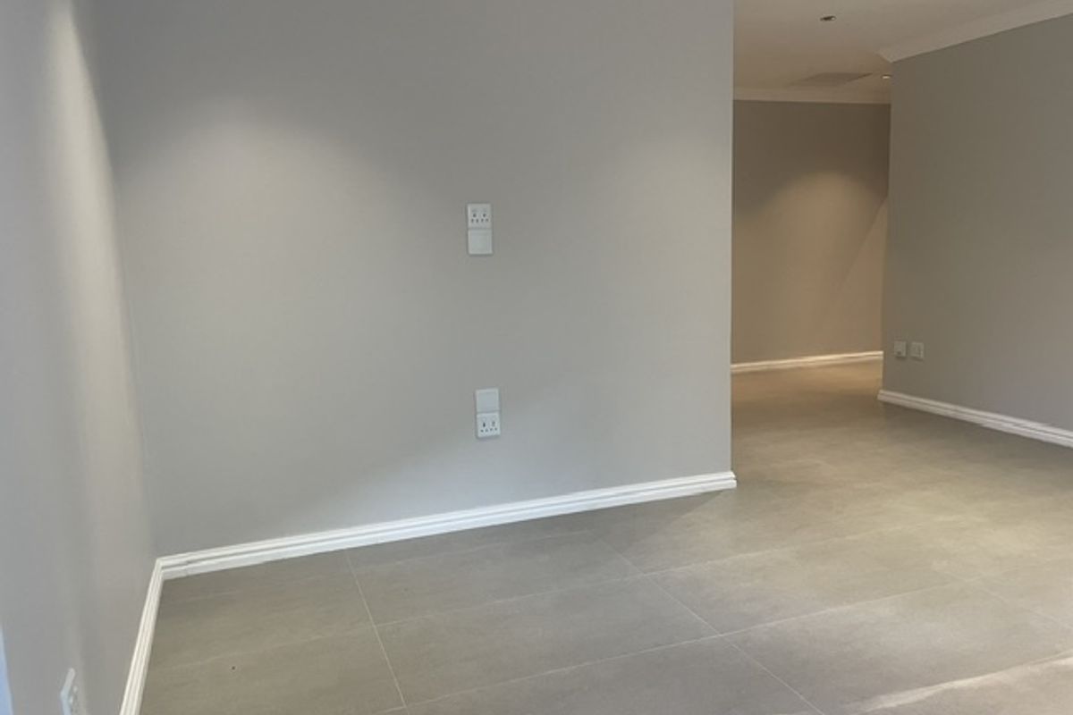 A bright, neutral-toned living area featuring modern large-format floor tiles, recessed downlighting, and clean architectural lines throughout the open-plan space.