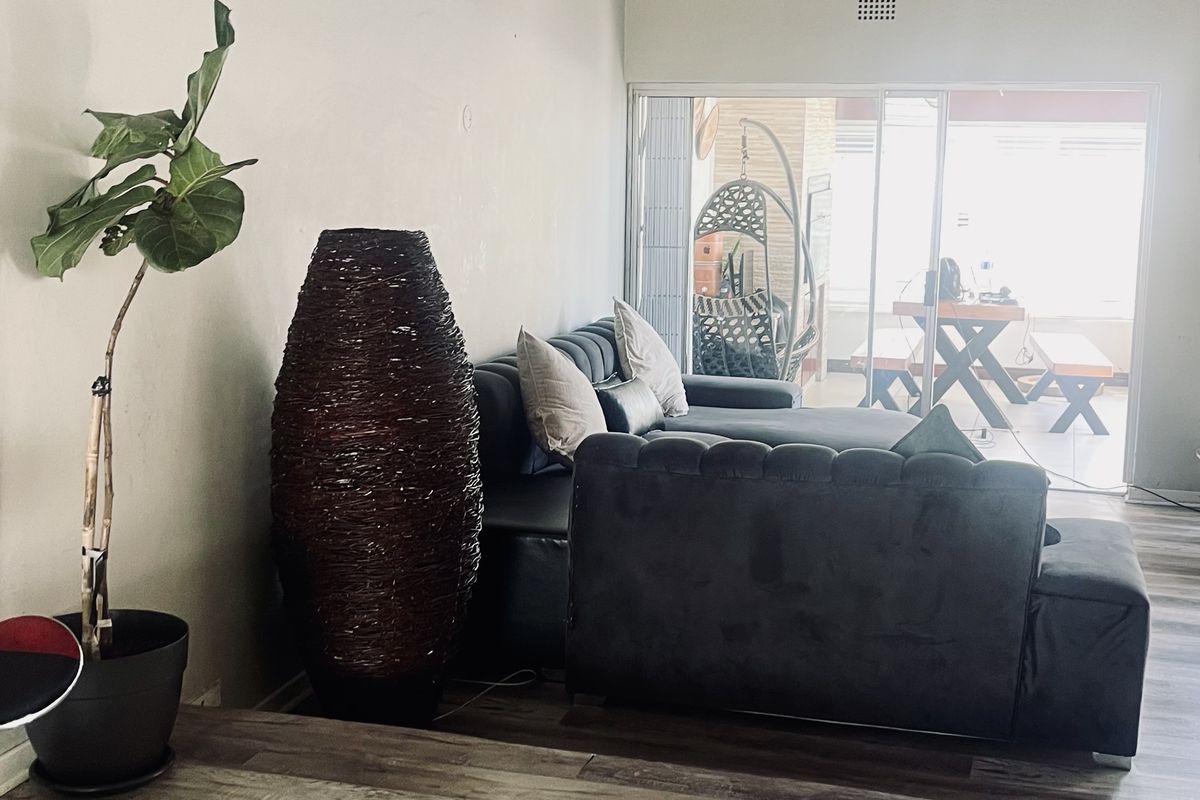 Spacious living room featuring high vaulted ceilings with exposed timber beams, modern laminate flooring, and large sliding glass doors leading to an outdoor patio area.