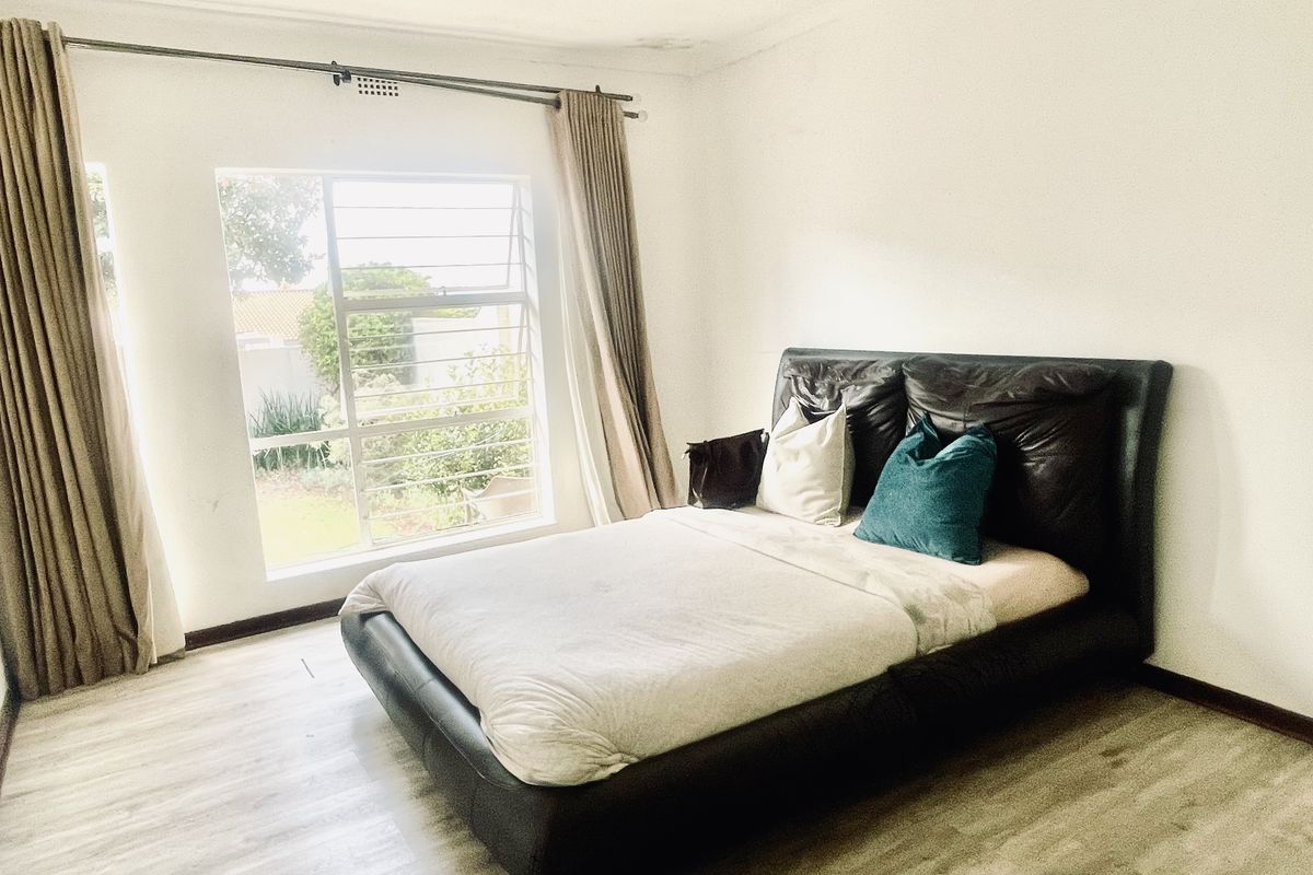 A bright bedroom featuring laminate flooring and a large window with garden views, providing a neutral canvas for personalization.