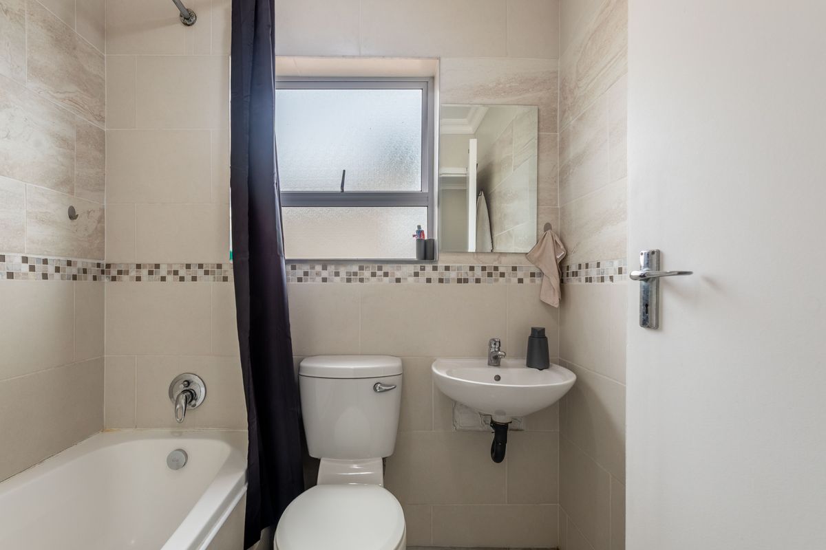 Compact bathroom featuring a bathtub with shower head, wall-mounted basin, and tiled walls with a decorative mosaic border.