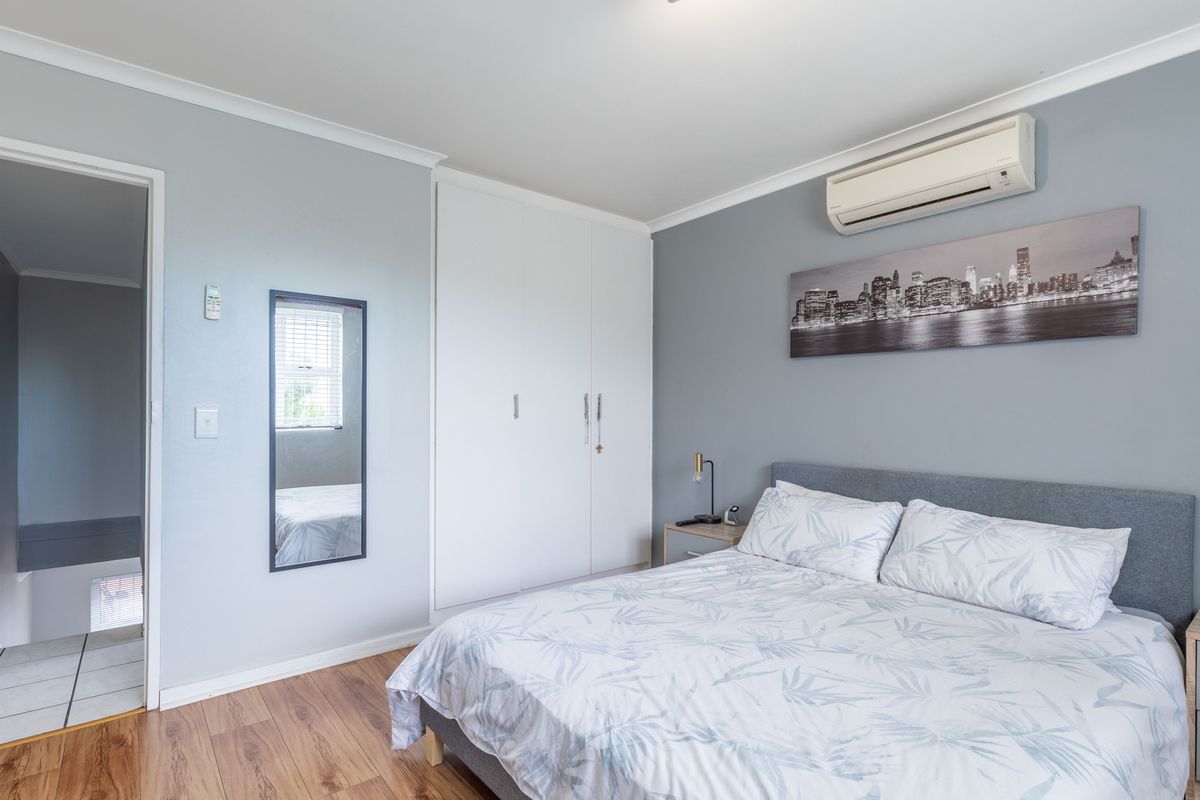 A well-maintained bedroom featuring built-in wardrobes, laminate flooring, and a wall-mounted air conditioning unit.