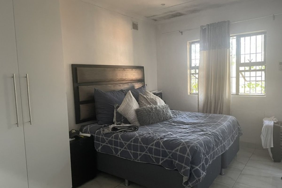A bedroom featuring built-in wardrobes, tiled flooring, and a window with security bars.