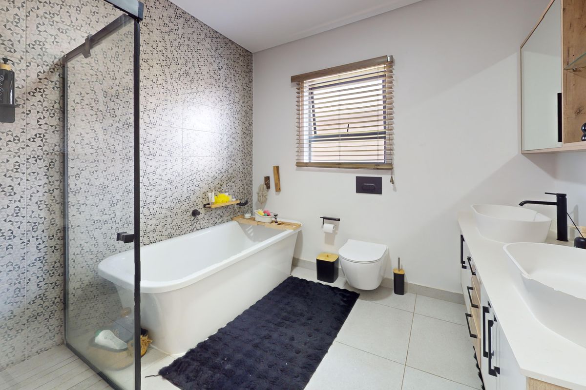 Modern bathroom featuring a freestanding bathtub, glass-enclosed shower, wall-mounted toilet, and a double vanity with vessel sinks and contemporary black fixtures.