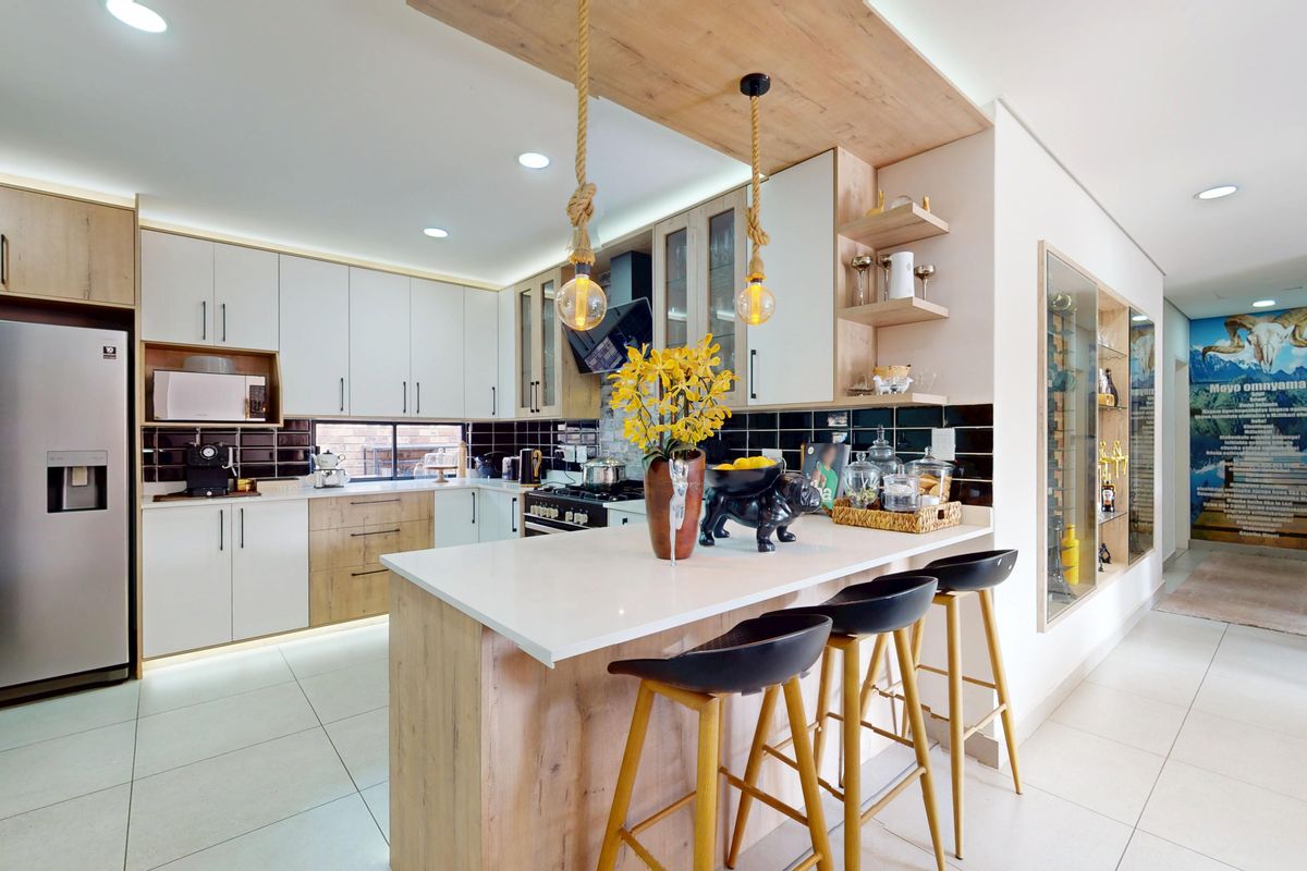 Modern kitchen featuring light wood and white cabinetry, stone countertops, a central island with breakfast bar, and integrated appliances with stylish under-cabinet lighting.