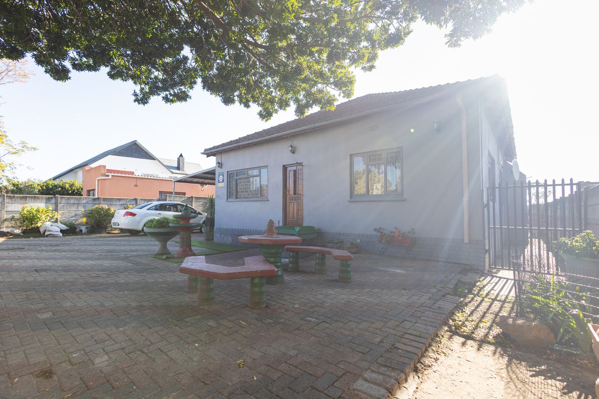 A view of the exterior side and rear area of the house, featuring paved ground and a secure metal gate.