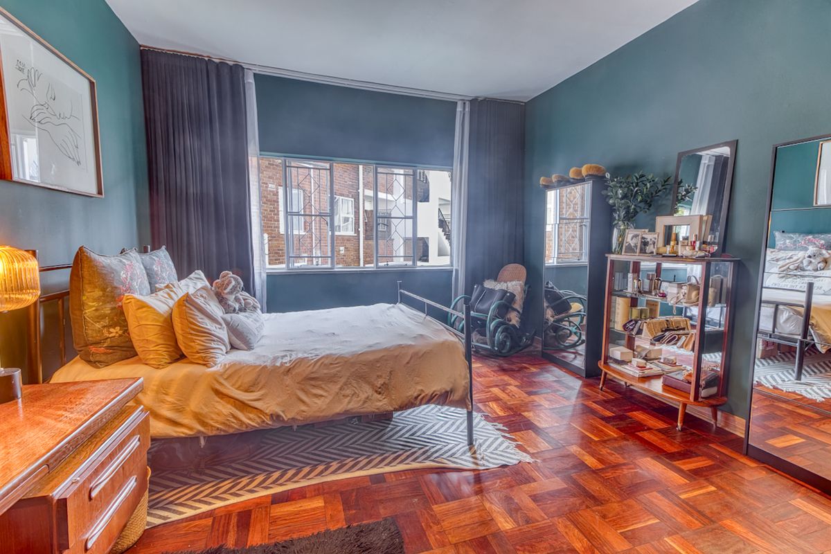 A well-maintained bedroom featuring classic parquet flooring and large steel-framed windows that provide natural light.