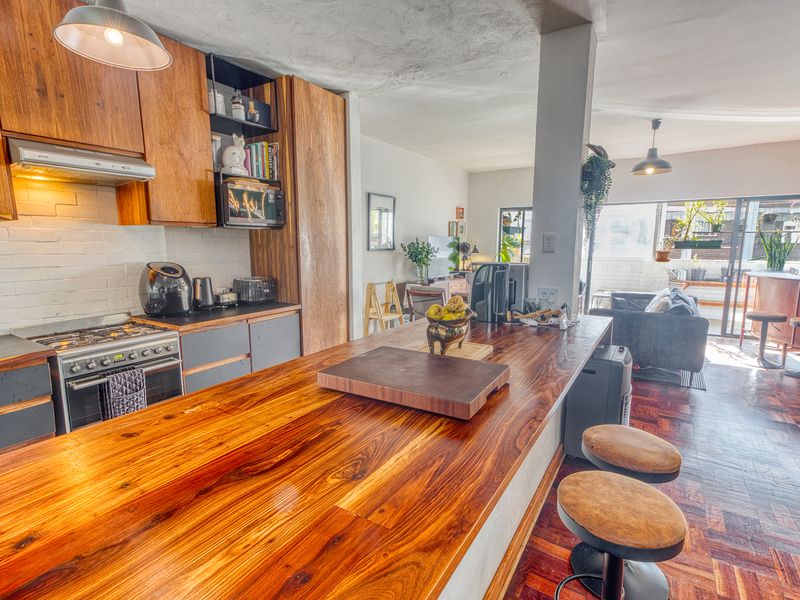 Open-plan kitchen and living area featuring a large wooden breakfast bar, gas stove, and parquet flooring, leading out to a balcony.