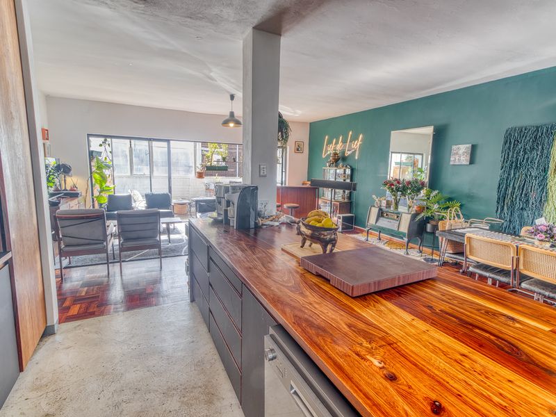 Spacious open-plan living area featuring a large timber kitchen island, parquet flooring, and seamless flow to an outdoor balcony through sliding glass doors.