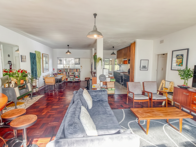 Spacious open-plan living and dining area featuring rich parquet flooring, a modern kitchen with integrated cabinetry, and a functional breakfast bar layout.