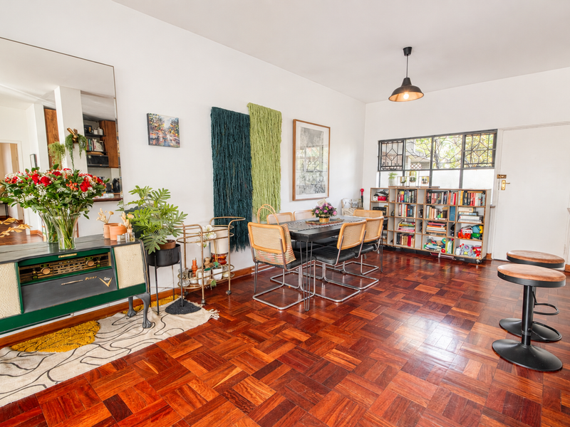A bright dining area featuring classic parquet flooring, a large wall mirror, and a pendant light, with access to an adjacent room.