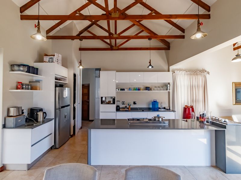 Modern kitchen featuring a large central island with stone countertops, sleek white cabinetry, and striking exposed timber roof trusses.