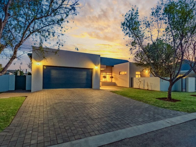 Modern single-story residential facade featuring a double garage, paved driveway, and well-maintained front garden at dusk.