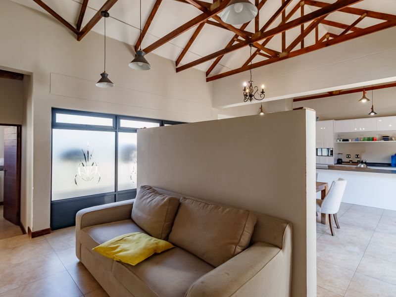 Spacious open-plan living and kitchen area featuring high vaulted ceilings with exposed timber trusses, tiled floors, and modern kitchen cabinetry.