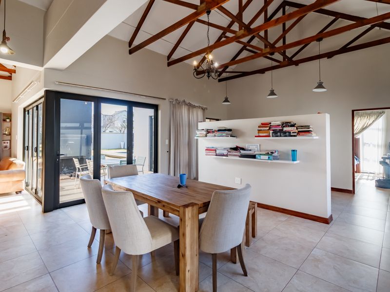Spacious open-plan living and dining area featuring high vaulted ceilings with exposed timber trusses, tiled floors, and large sliding doors leading to the patio.