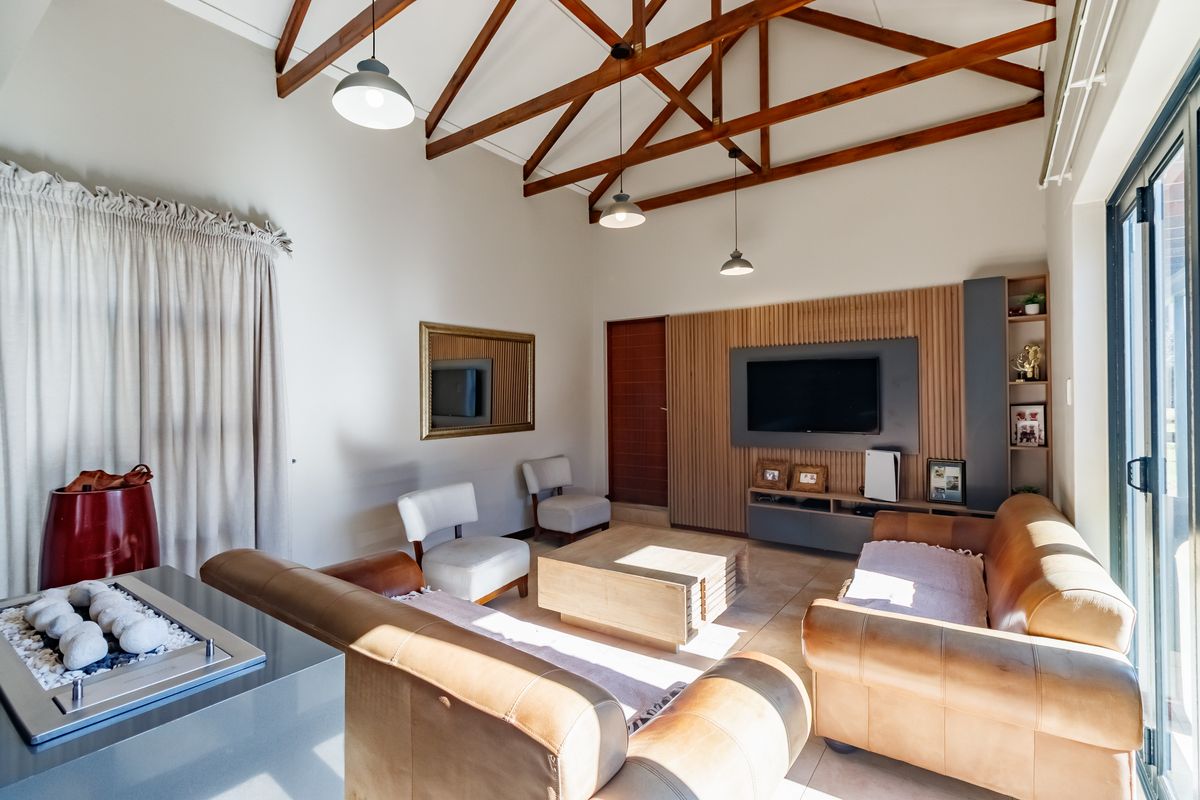 Spacious living room featuring high vaulted ceilings with exposed timber trusses, a modern built-in media wall, and large sliding doors providing natural light.