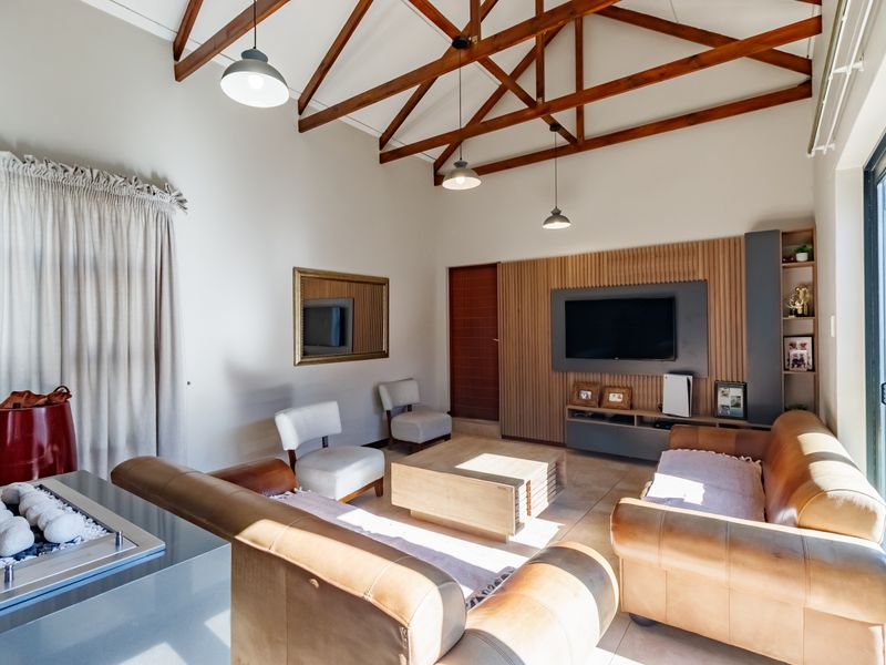 Spacious living room featuring high vaulted ceilings with exposed timber trusses, a modern built-in media wall, and large sliding doors providing natural light.
